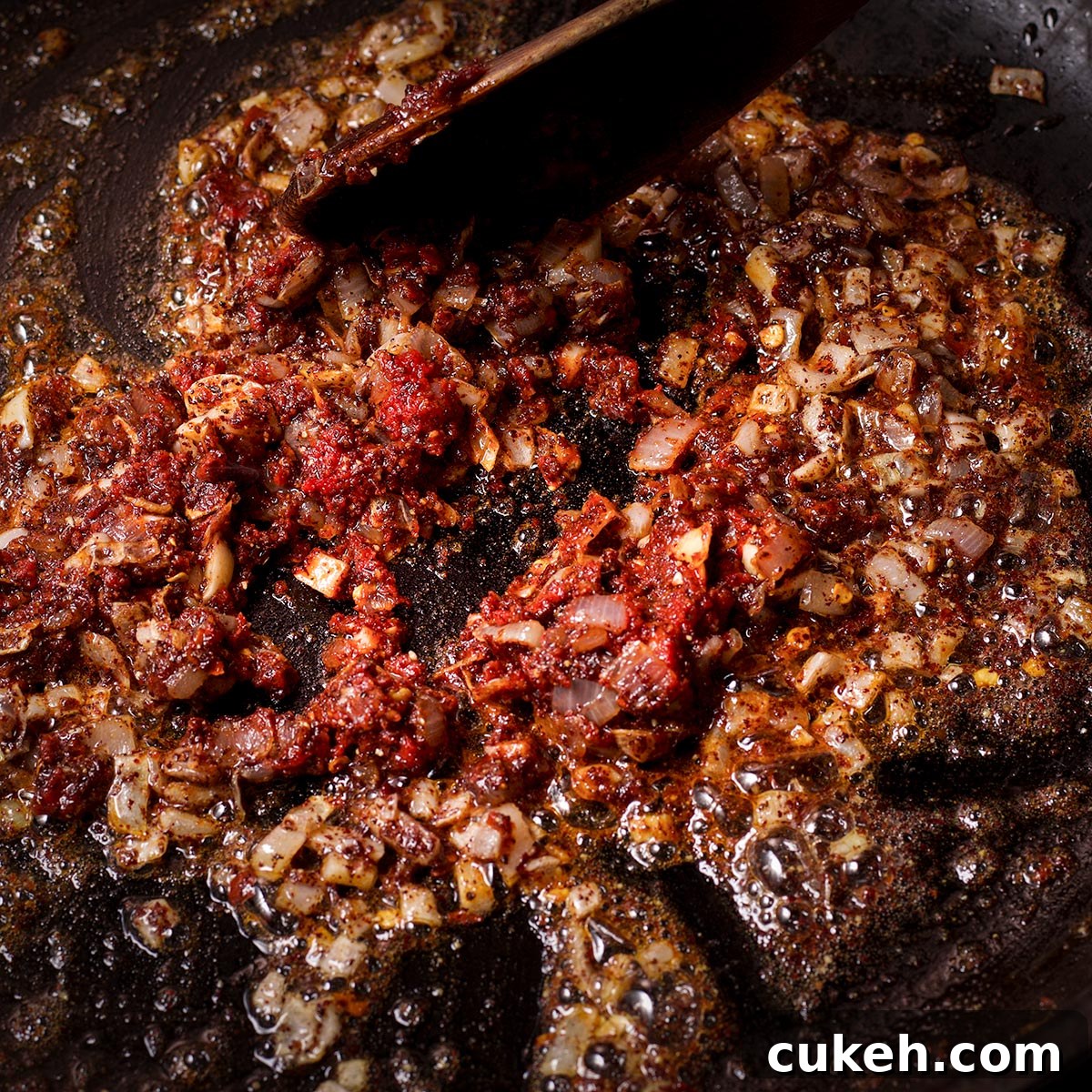 Adding tomato paste and spices to the skillet and using a wooden spoon to stir them into the mushrooms.