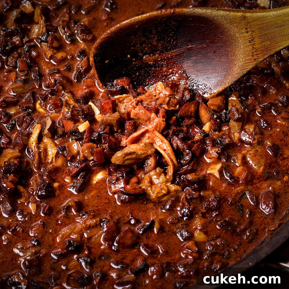 Using a wooden spoon to stir the mushrooms and the reserved mushroom soaking liquid into the shallot and spice mixture.