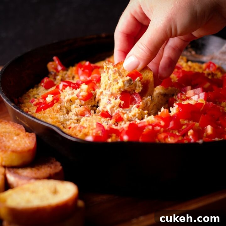 Someone dipping a toasted slice of bread into a cast iron skillet filled with cheesy hot mushroom dip.