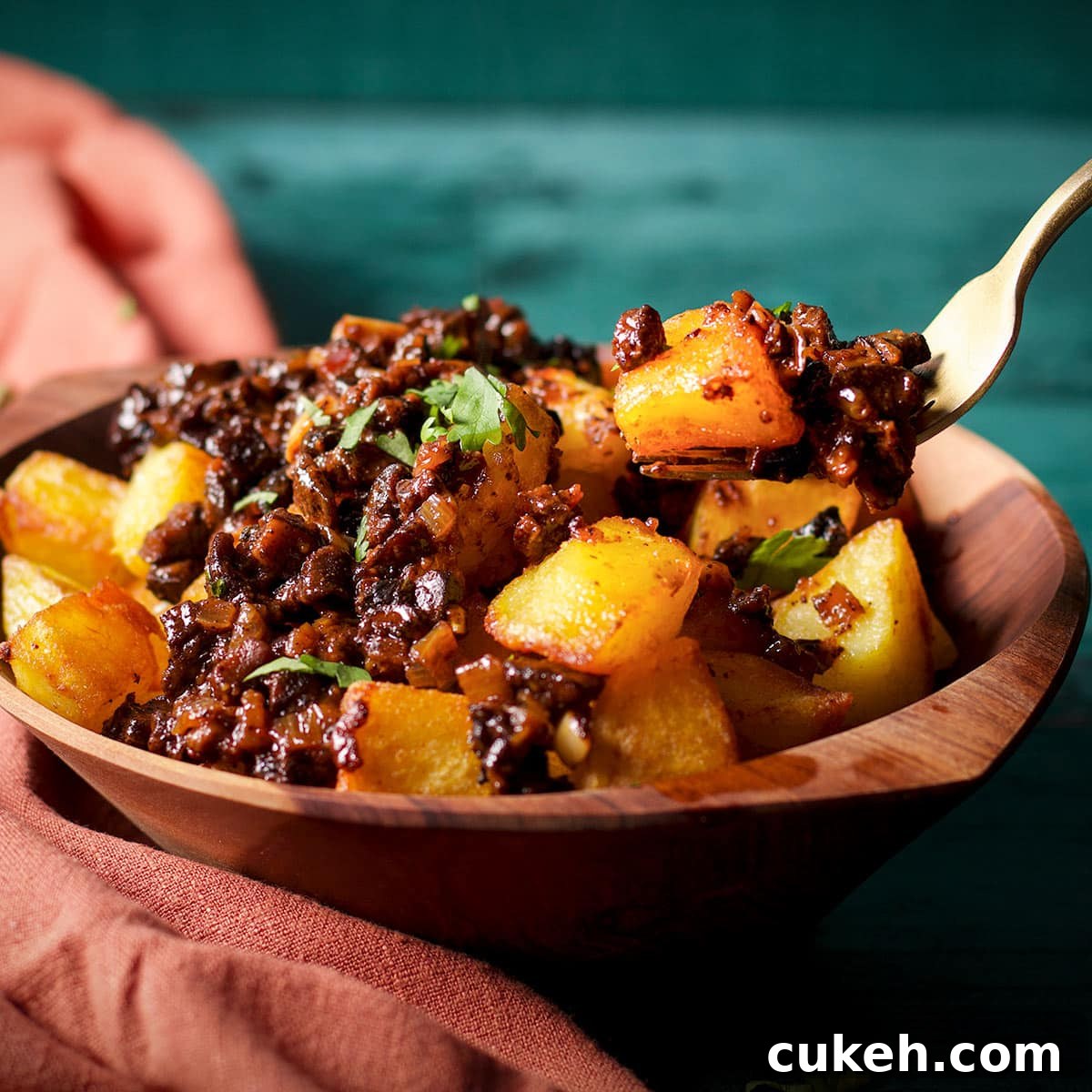 Someone using a fork to lift a bite of crispy fried potatoes topped with mushroom ragu.