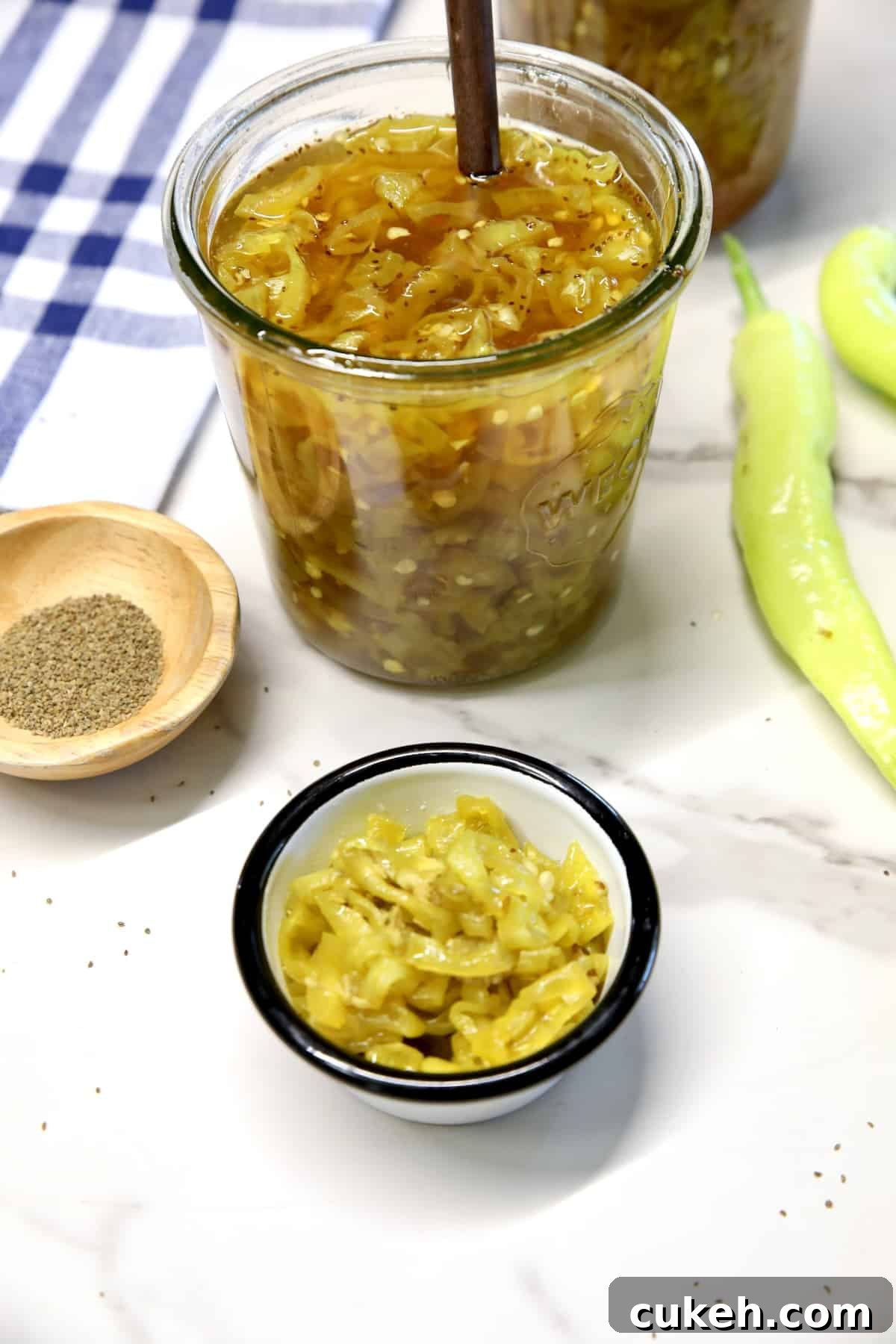 Banana peppers in a jar with fork, small bowl, bowl of celery seeds.