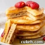 gluten free pancakes in a stack with a piece cut out and strawberries on top with maple syrup being poured on