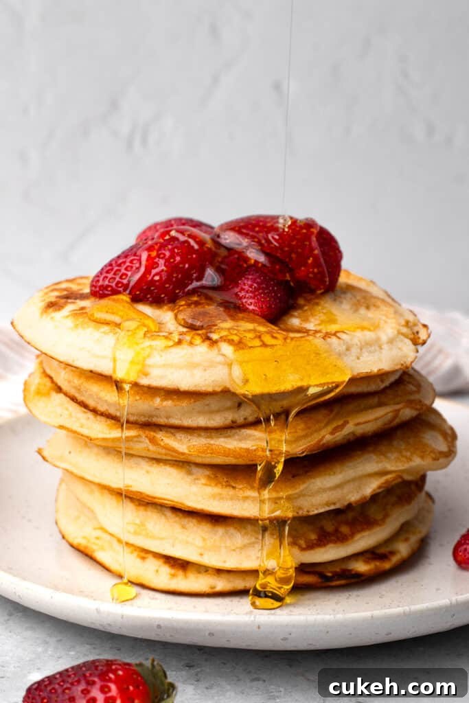 Gluten free pancakes in a stack with syrup being poured over it and strawberries
