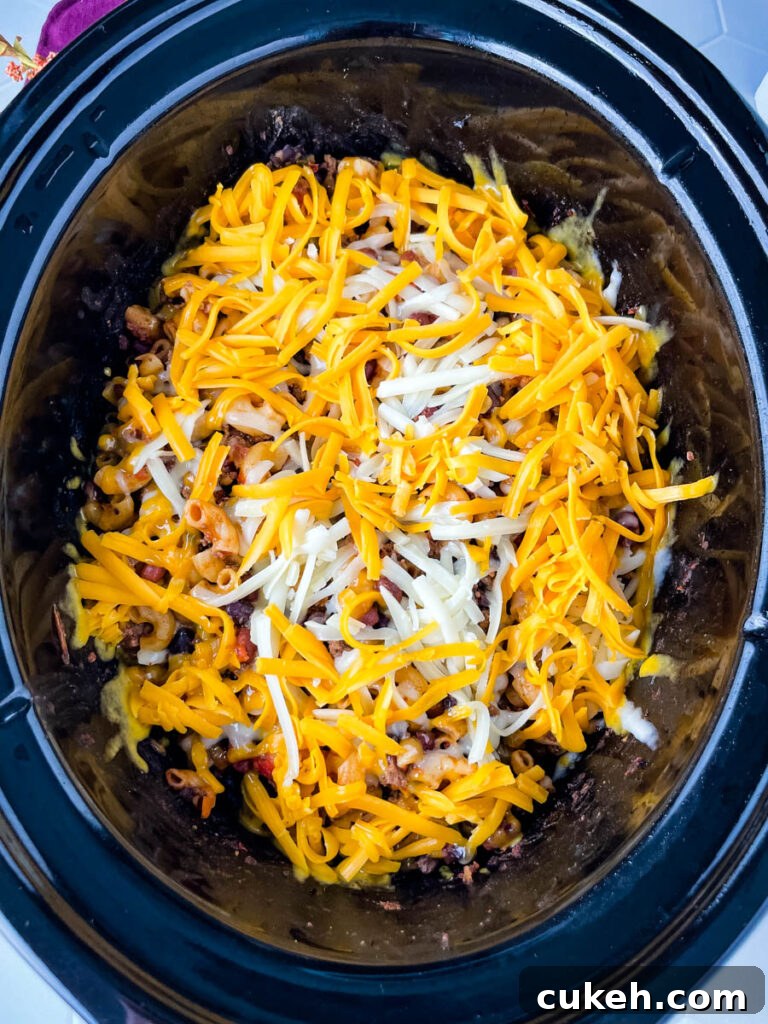 uncooked chili mac and cheese in a slow cooker topped with cheese