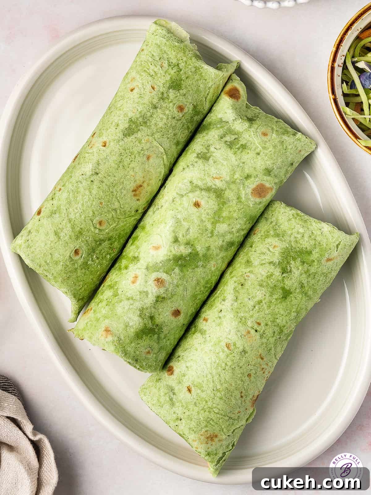 3 spinach flour tortilla burritos on white platter