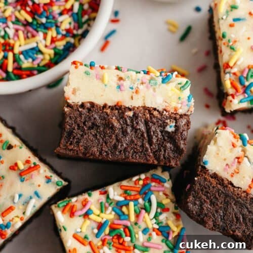 Brownies with an edible cookie dough layer with rainbow sprinkles on parchment paper.