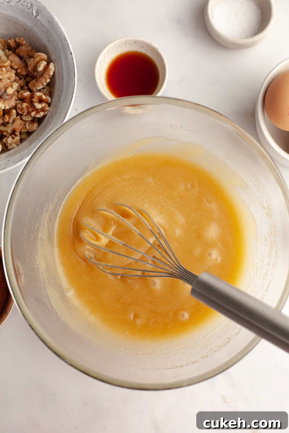 A glass bowl with a whisk and a yellow mixture in it.