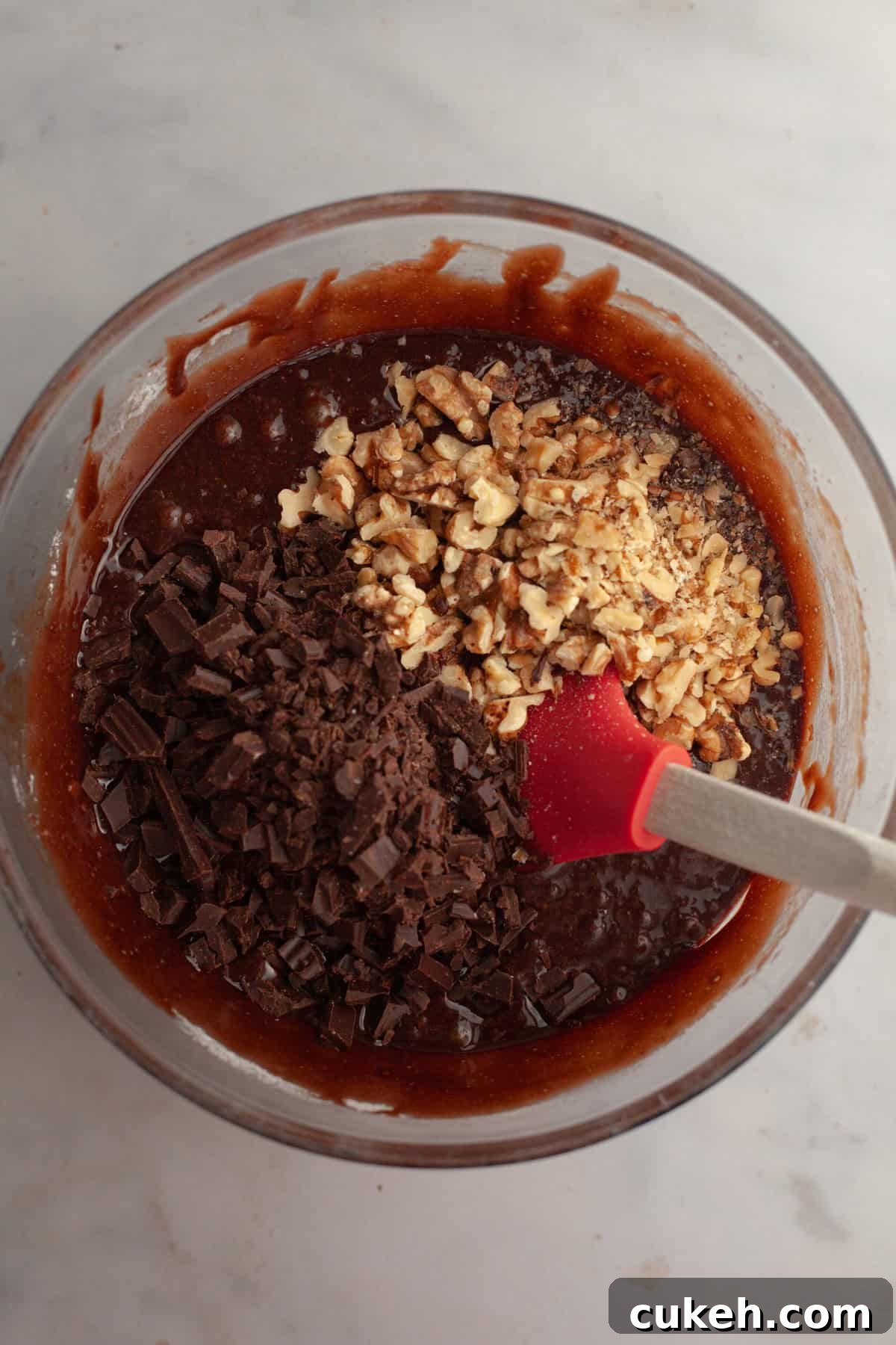 Brownie batter in a glass bowl with chopped chocolate and toasted walnuts.