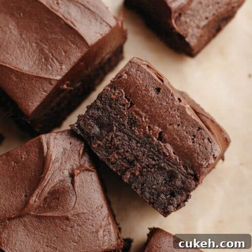 Brownies covered in chocolate cream cheese frosting on parchment paper.