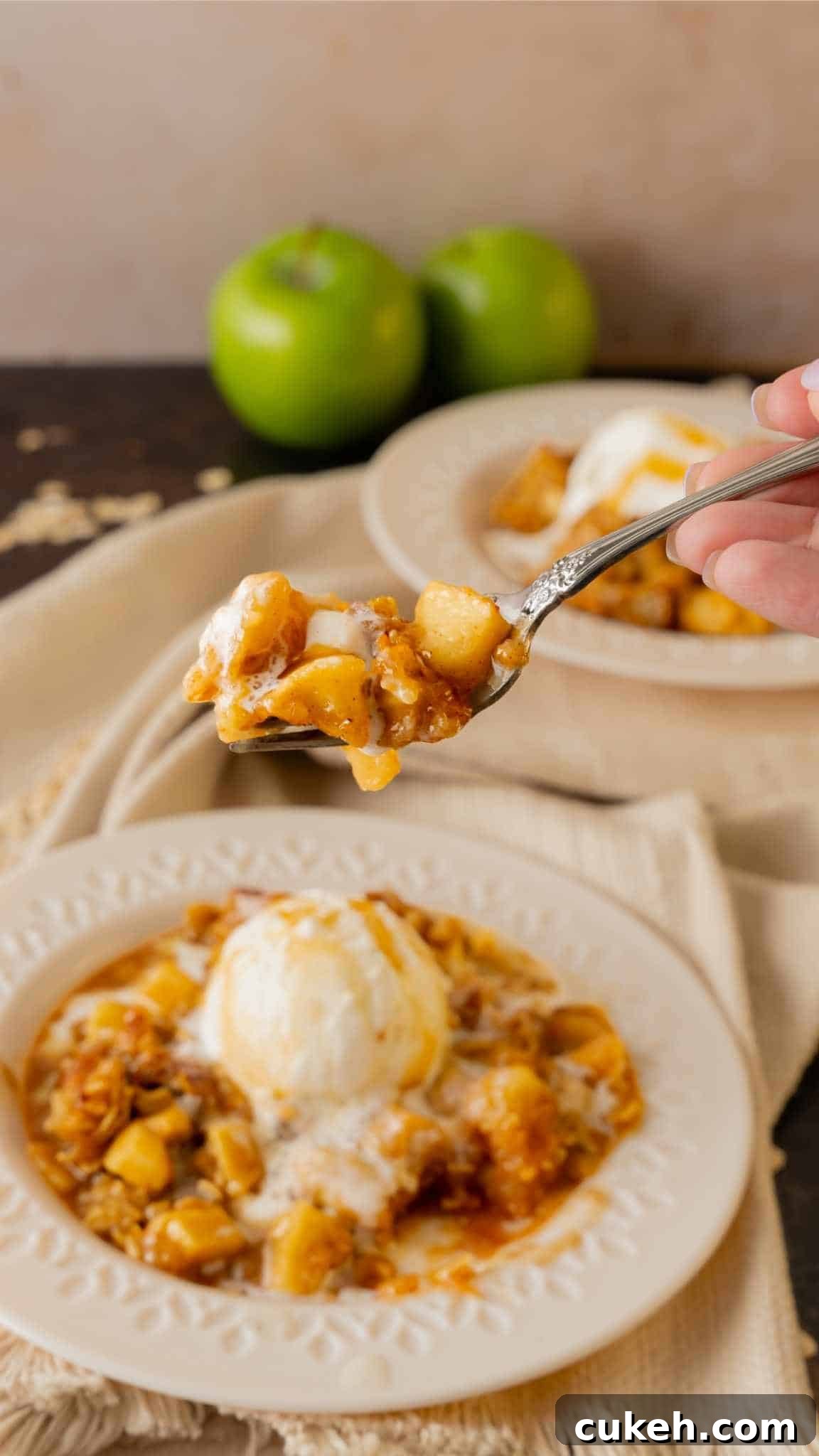 A fork with apple crisp and ice cream above a plate.
