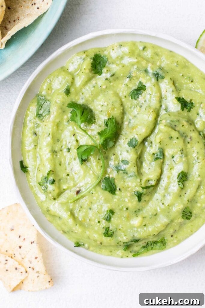 A bowl of creamy tomatillo avocado salsa verde shown being served with chips.