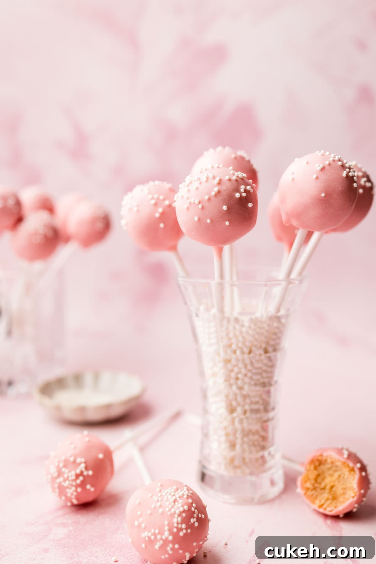 Starbucks-Style Gluten-Free Cake Pops Recipe 2 Pink Gluten-Free Cake Pops with white sprinkles on a small vase on pink background.
