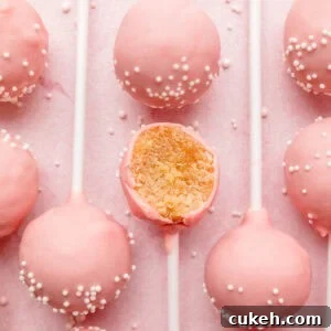 Starbucks-Style Gluten-Free Cake Pops Recipe 12 Several gluten-free pink cake pops lined up on pink surface, one with bite taken.