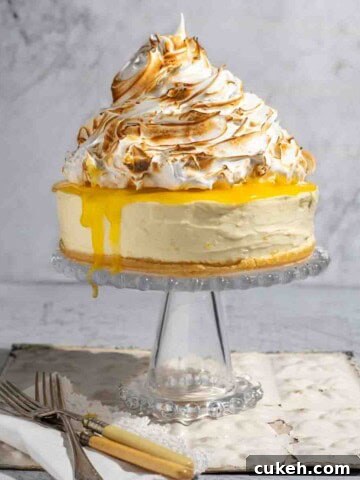 Lemon meringue cheesecake on a glass cake stand.
