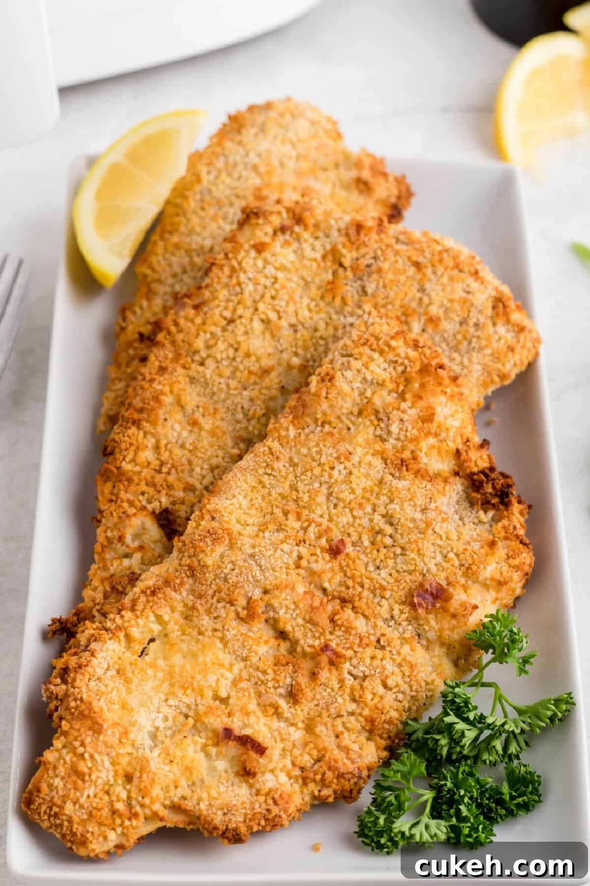 Reheated fish in the air fryer and served on a white plate with a slice of lemon. 