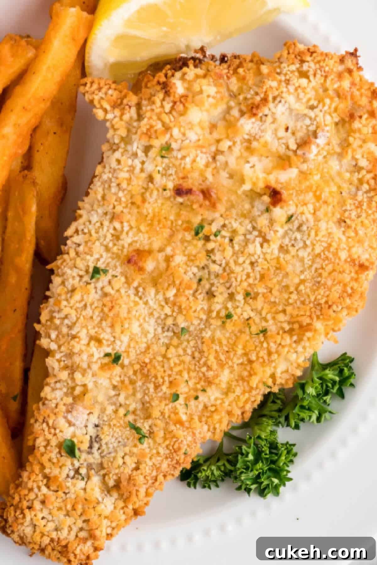 Fish reheated in air fryer and then served on a white plate with french fries and a slice of lemon. 