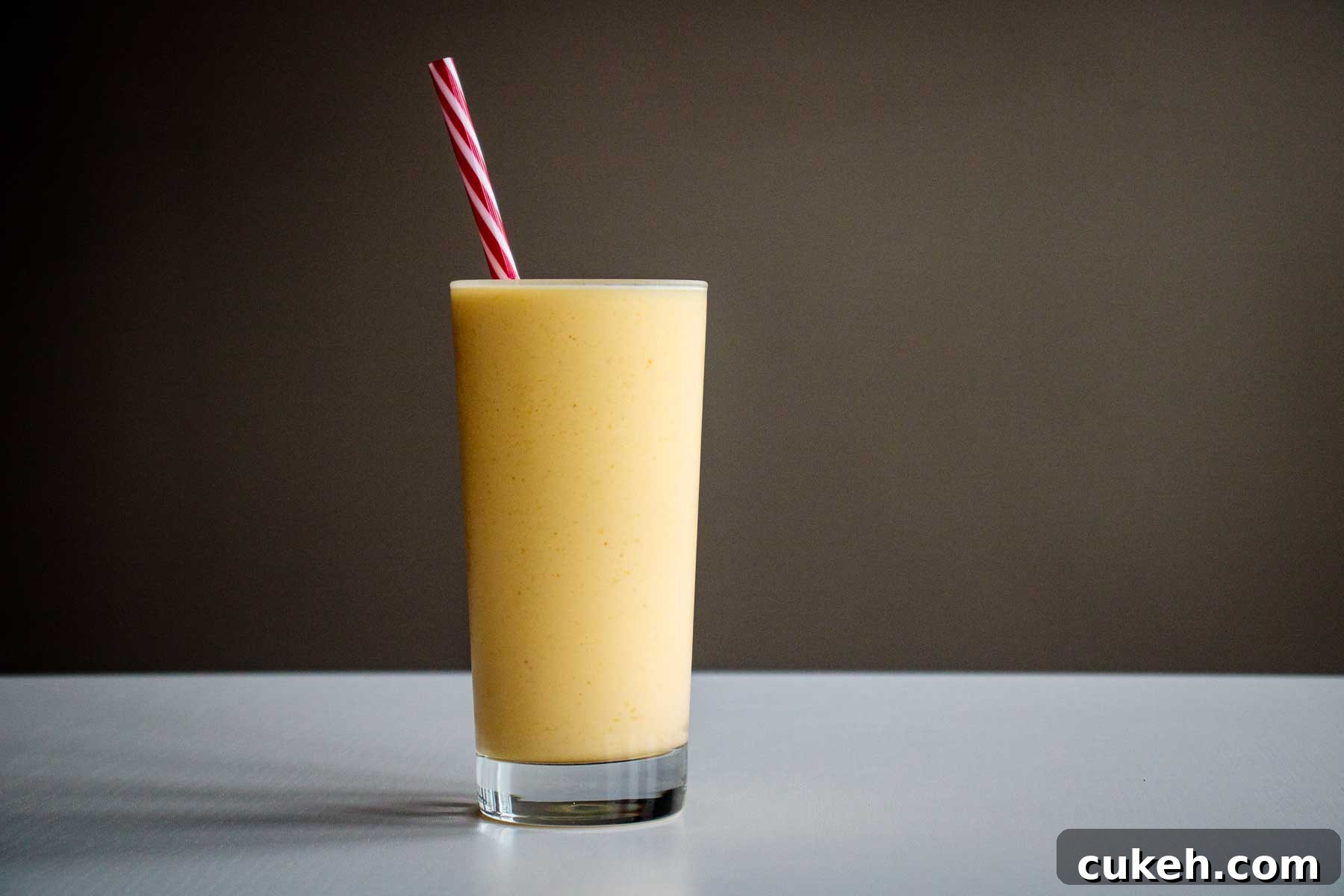 mango smoothie served in a tall glass cup with reusable red straw