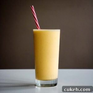 mango smoothie in a tall glass cup with reusable red straw