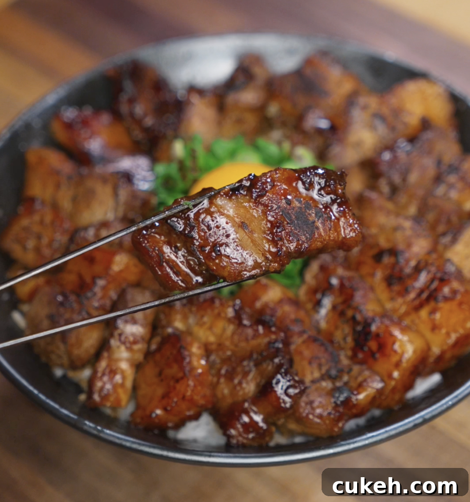 Sticky Glazed Pork Belly Bites: Sweet Savory Crispy Recipe 3 A glossy piece of caramelized pork belly is held up with chopsticks over the rice bowl, showcasing its seared edges and sticky glaze.