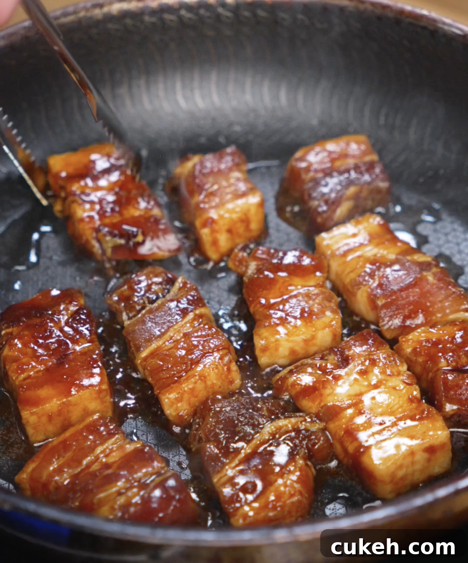 Sticky Glazed Pork Belly Bites: Sweet Savory Crispy Recipe 5 Pork belly pieces sizzle in a hot skillet, forming a deep brown crust as the glaze thickens and caramelizes around each bite.