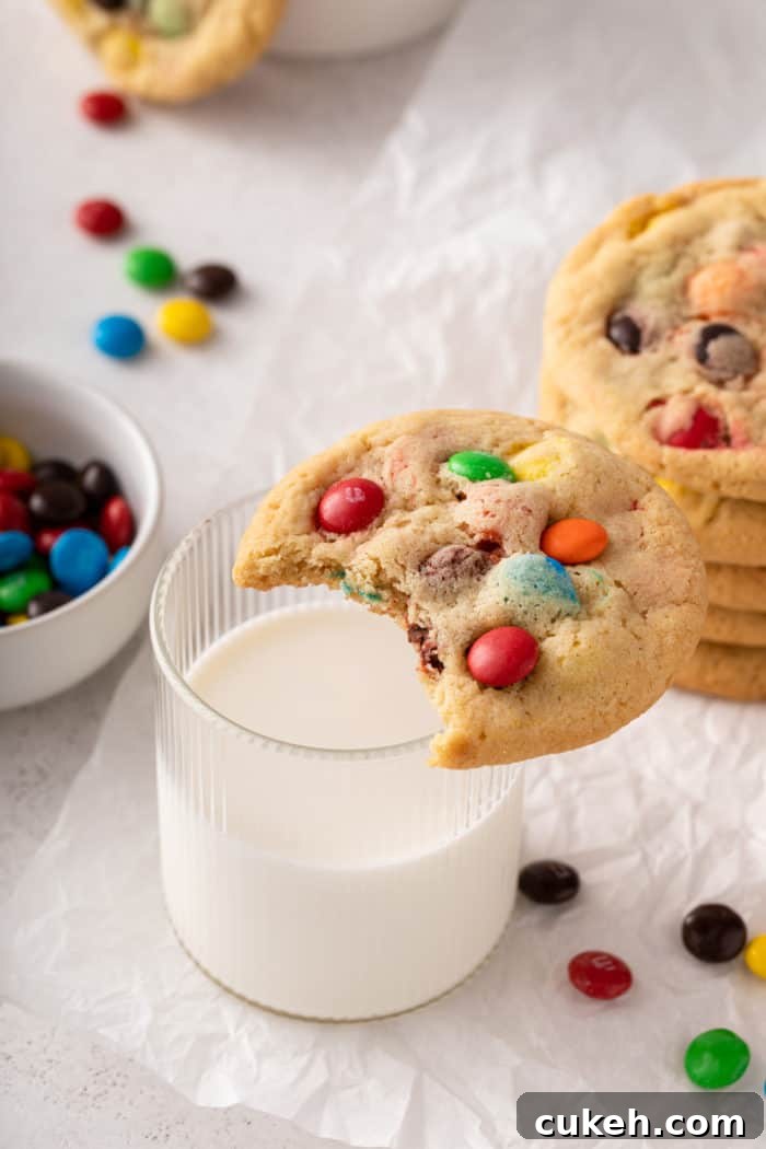 M&M cookie with a bite taken out of it set on the edge of a glass of milk.