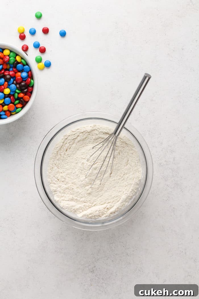 Dry ingredients for M&M cookies being whisked together in a glass bowl.