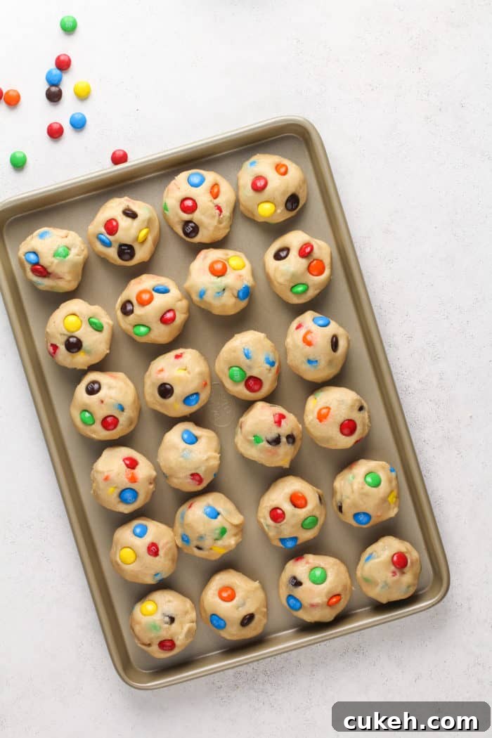 Balls of m&m cookie dough set on a baking sheet to chill.