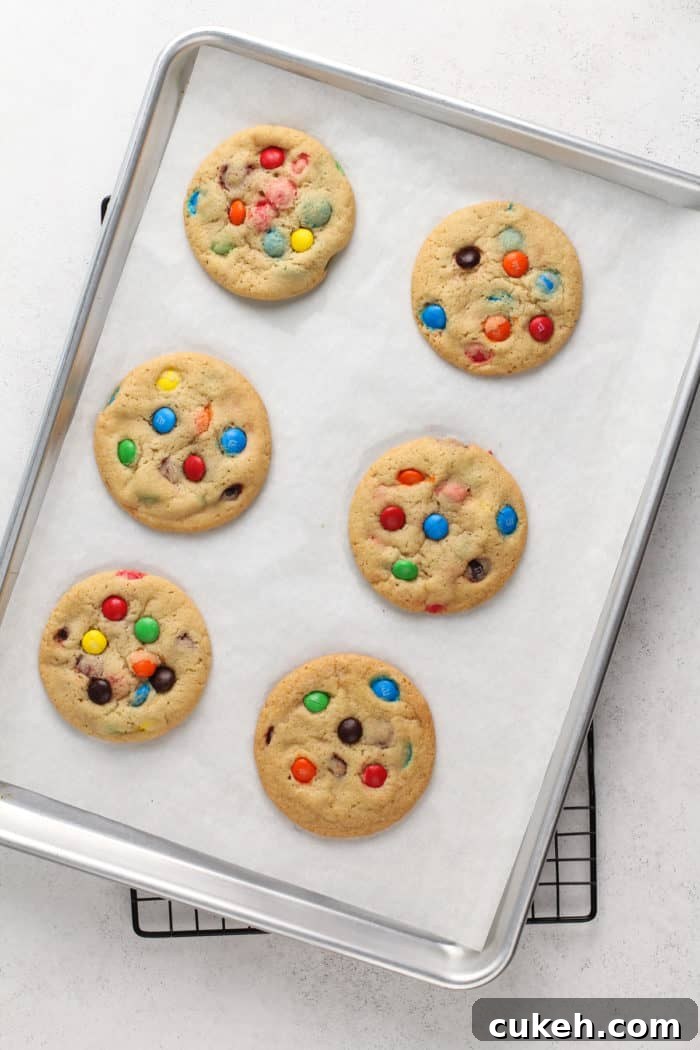 6 baked m&m cookies on a parchment-lined baking sheet.