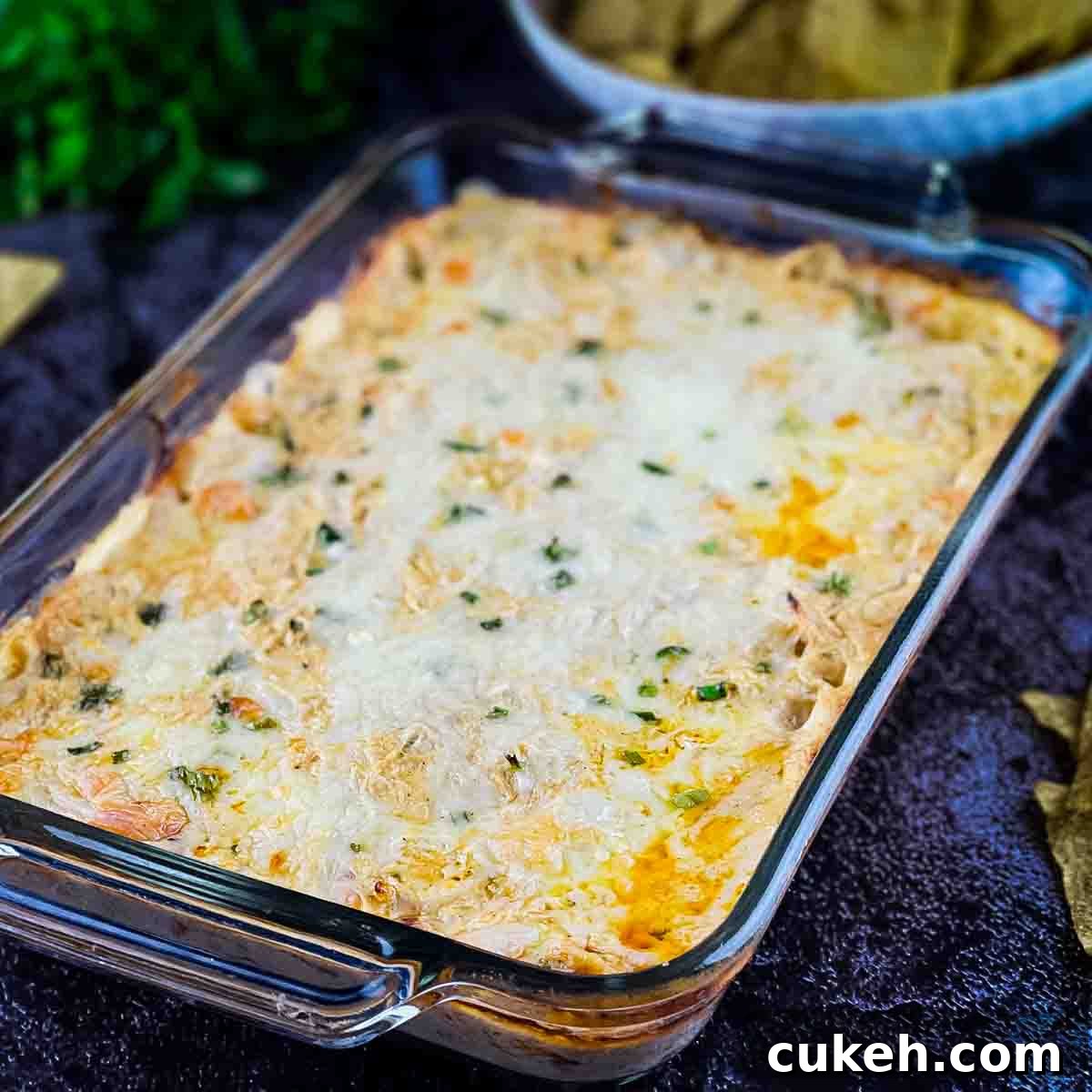 Buffalo Chicken Dip without Cream Cheese — Tangy, Cheesy Recipe 10 The baked buffalo chicken dip in a casserole dish, with a bowl of tortilla chips in the background.