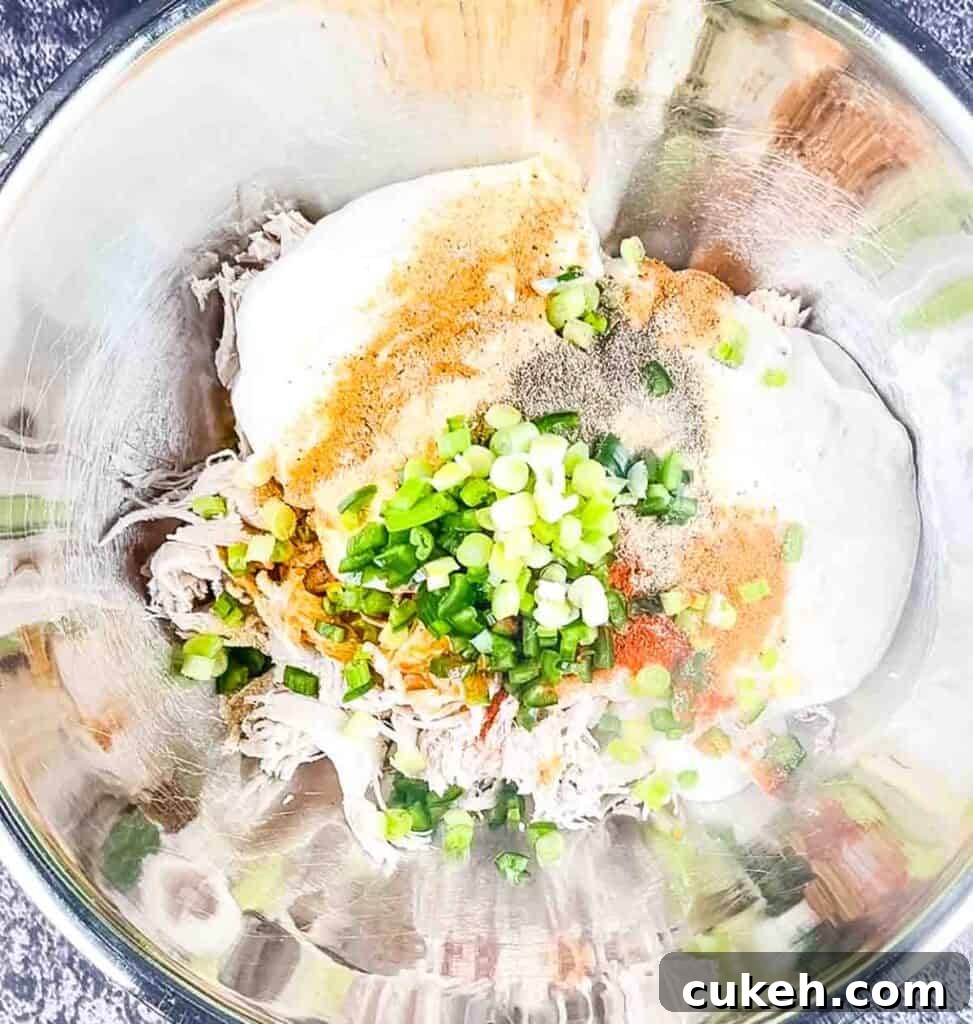 Buffalo Chicken Dip without Cream Cheese — Tangy, Cheesy Recipe 4 The shredded chicken in a bowl with sour cream, seasoning, hot sauce, and ranch dressing.