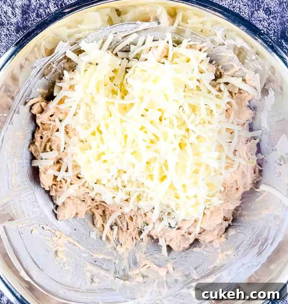 Buffalo Chicken Dip without Cream Cheese — Tangy, Cheesy Recipe 6 Shredded cheese added to the chicken in a bowl with sour cream, seasoning, hot sauce, and ranch dressing.
