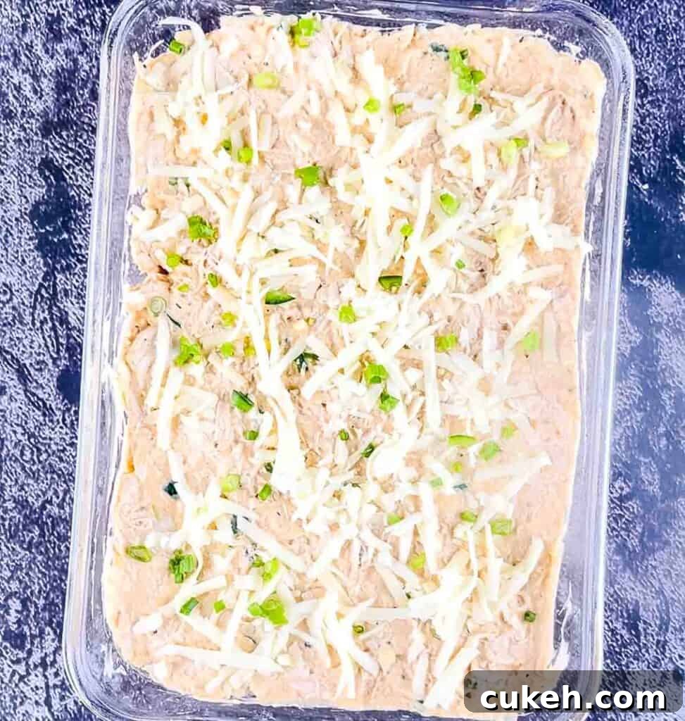 Buffalo Chicken Dip without Cream Cheese — Tangy, Cheesy Recipe 9 The buffalo chicken dip topped with extra shredded cheese and diced green onion in a glass casserole dish.