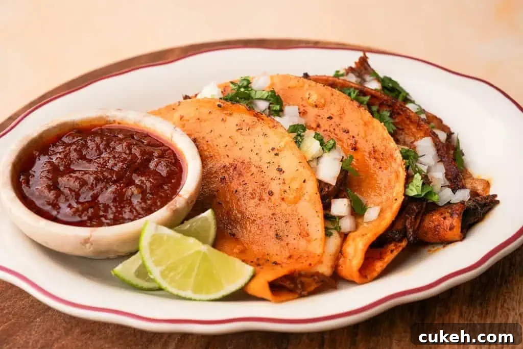Crispy birria tacos filled with shredded beef and cheese, served with consommé for dipping and lime wedges on the side.