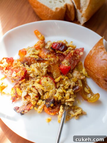 scrambled eggs and seared bell peppers with a side of bread on a plate