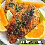 two perfectly cooked chicken breasts, marinated in citrus marinade. Plated and surrounded by slices of orange, lemon and lime.