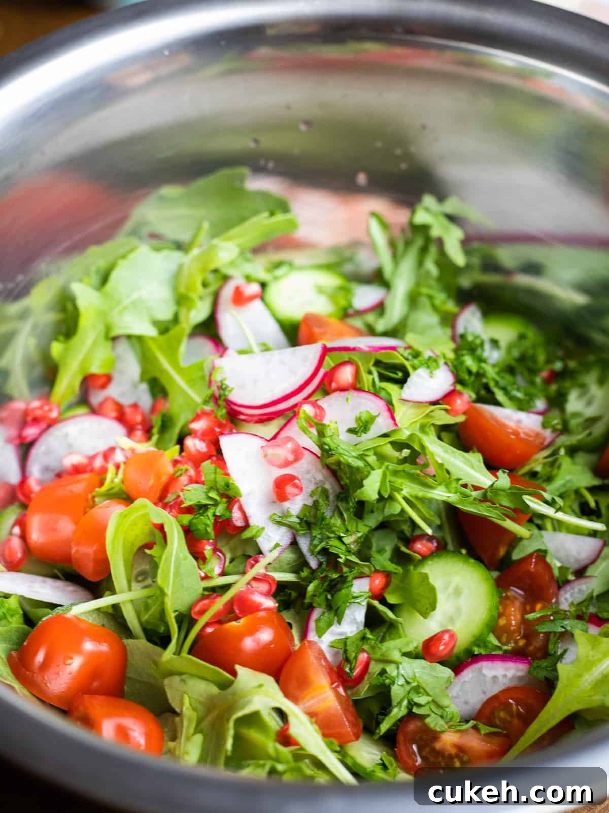 Photo of a metal bowl with the ingredients for rocket salad with sumac and pomegranate.