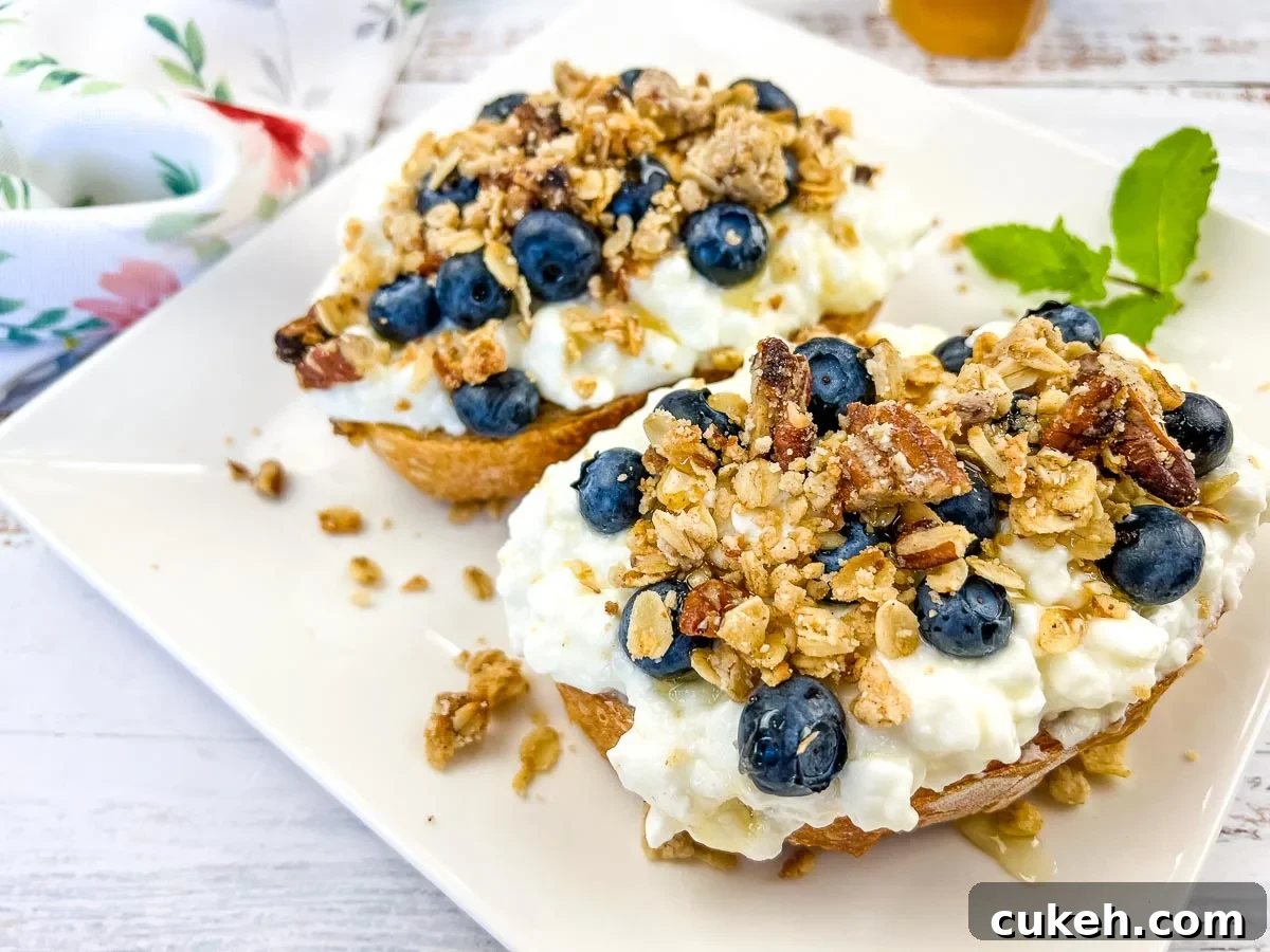 A plate of cottage cheese toast with blueberries, next to a honey dipper.