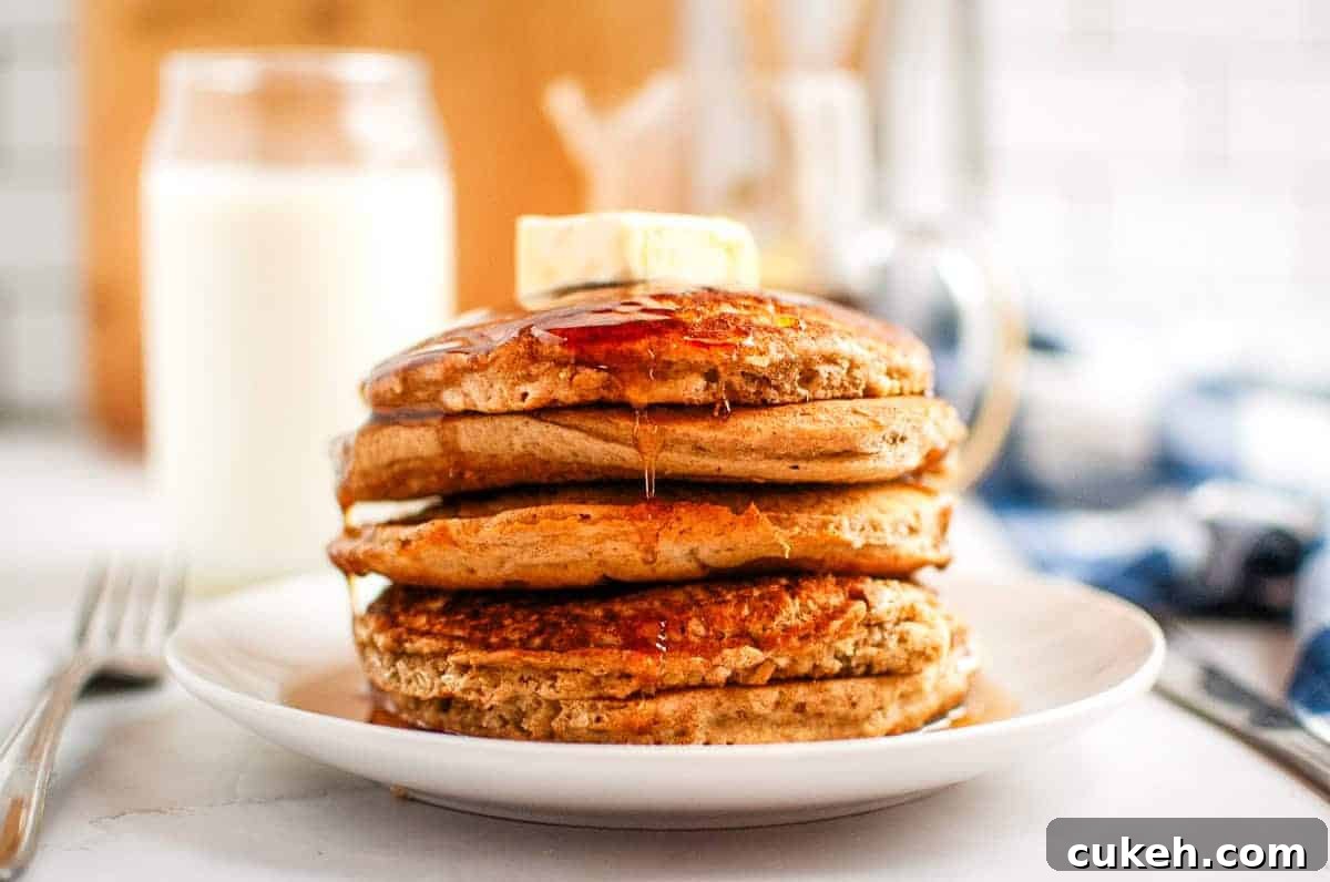 A stack of Buttermilk Oatmeal Pancakes with syrup and a pat of butter on top, served on a white plate.
