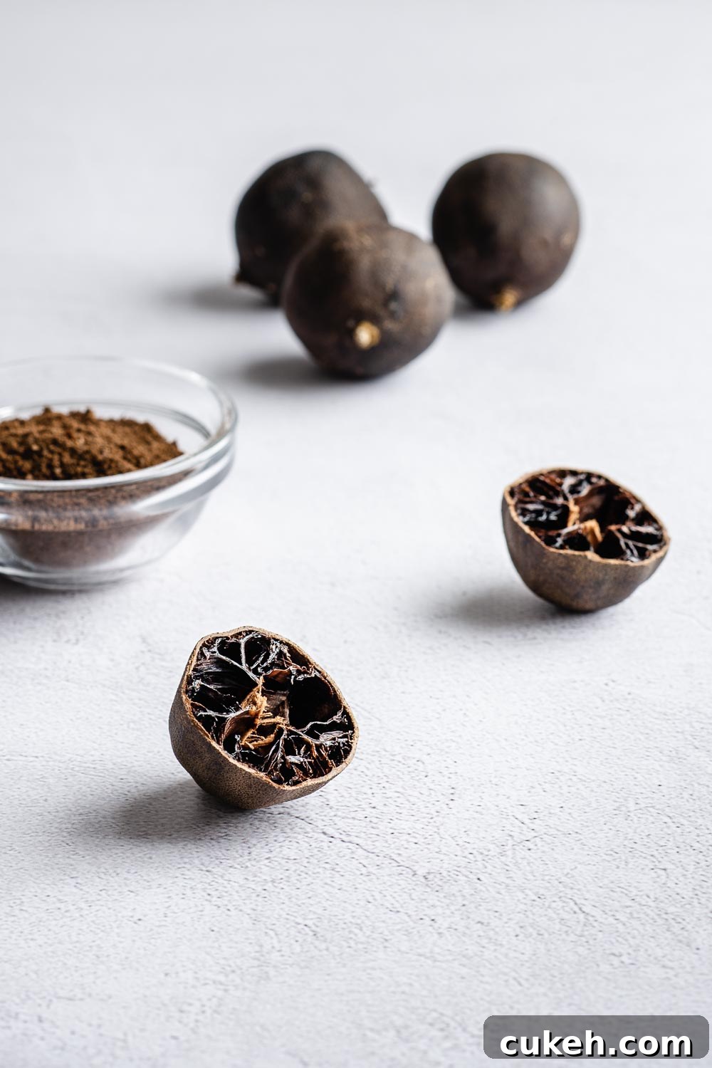 Black lime powder with sliced and whole dried black limes an a light concrete surface.