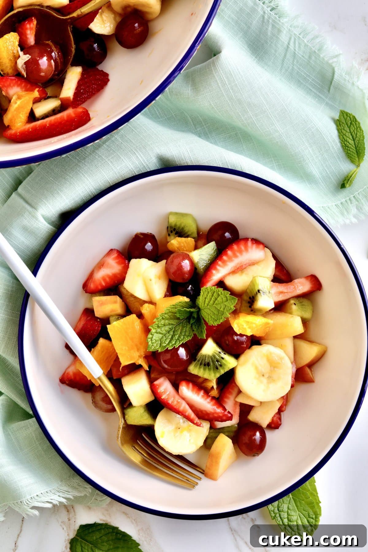 Italian Fruit Salad Recipe (Macedonia di Frutta)- in a bowl with a fork in it ready to eat. Big bowl of fruit salad in background.