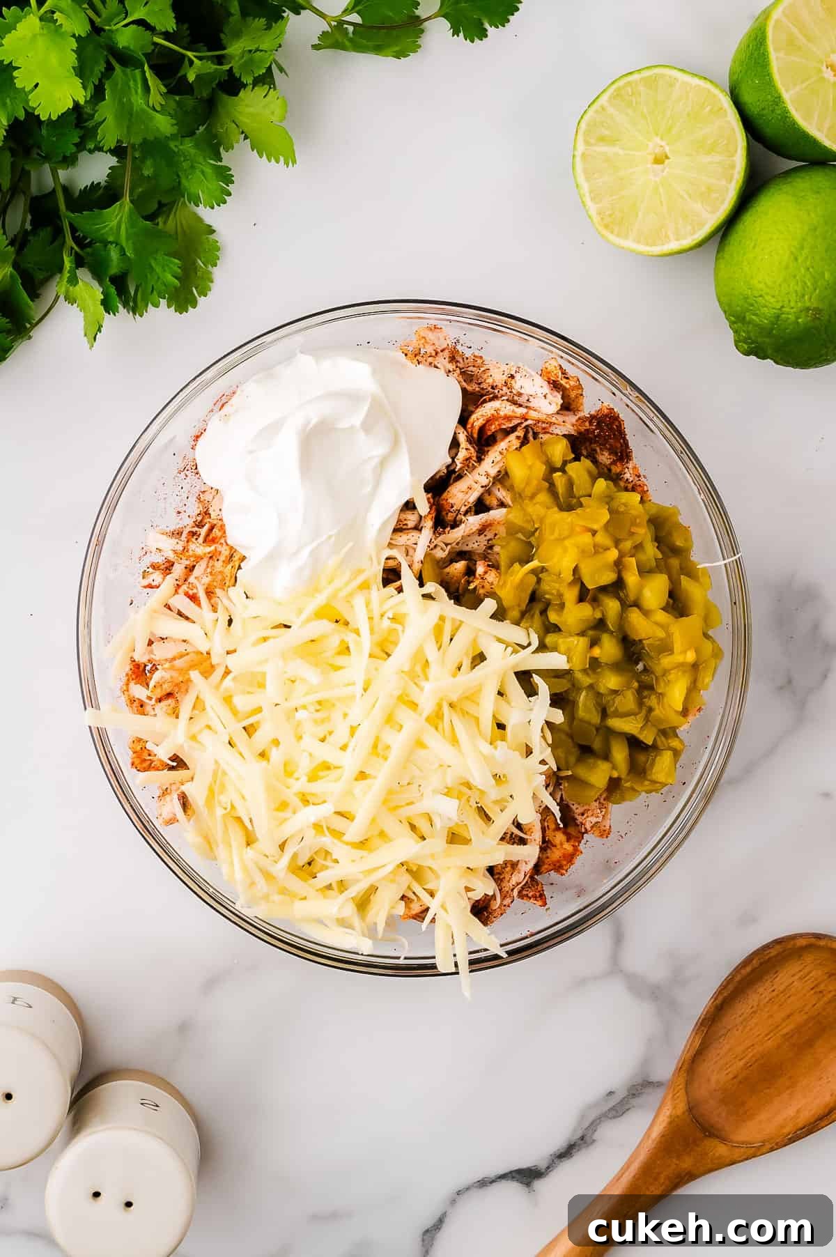 Shredded chicken, taco seasoning, cheese, sour cream and green chilis in a mixing bowl.