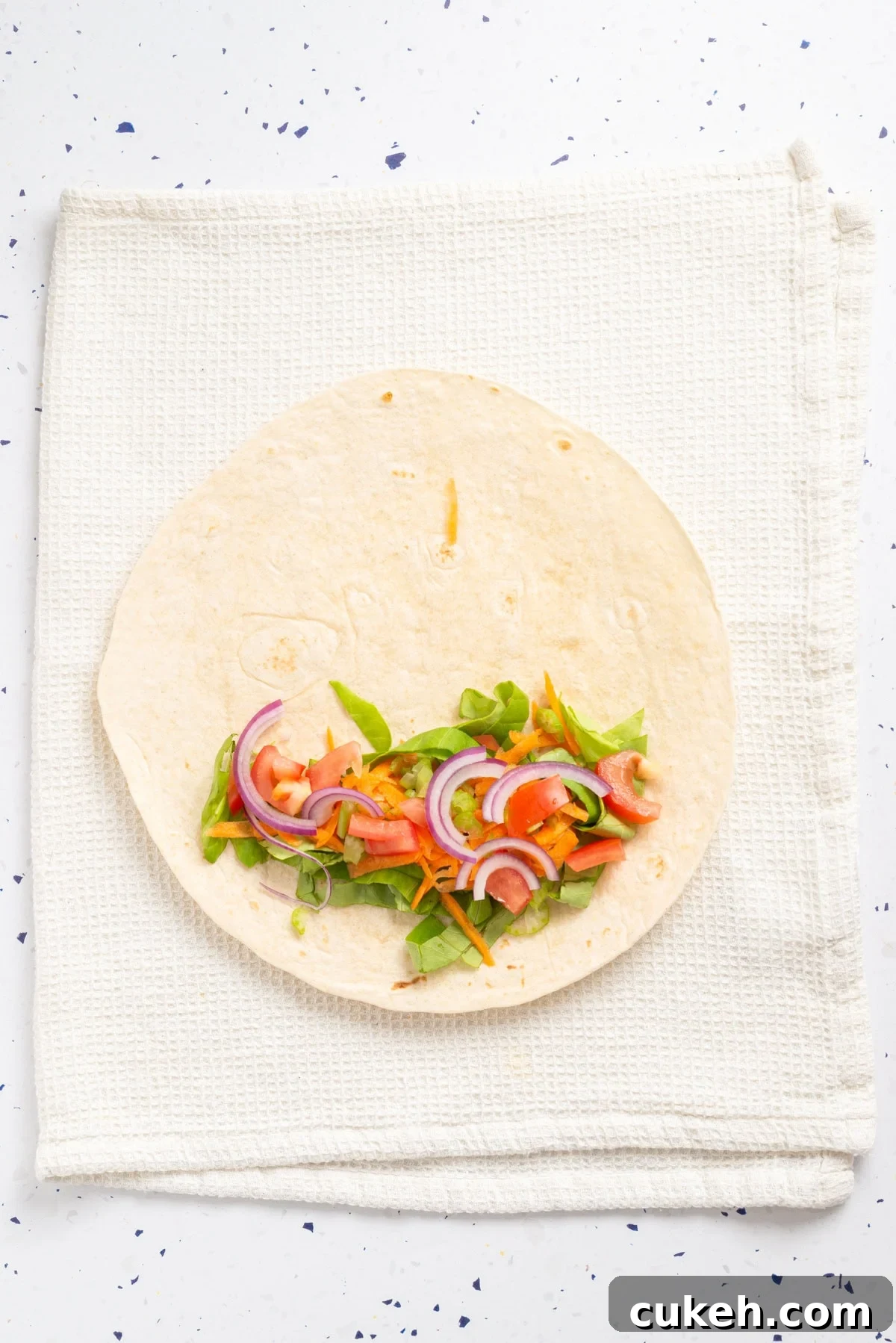 An overhead image of placing onions and tomatoes on tortillas.