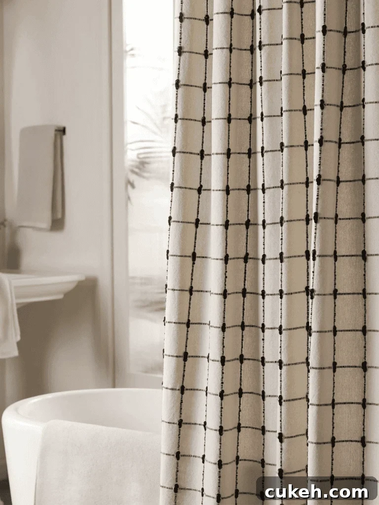 Beige shower curtain with a black grid pattern hanging beside a white bathtub in a bright, modern bathroom.