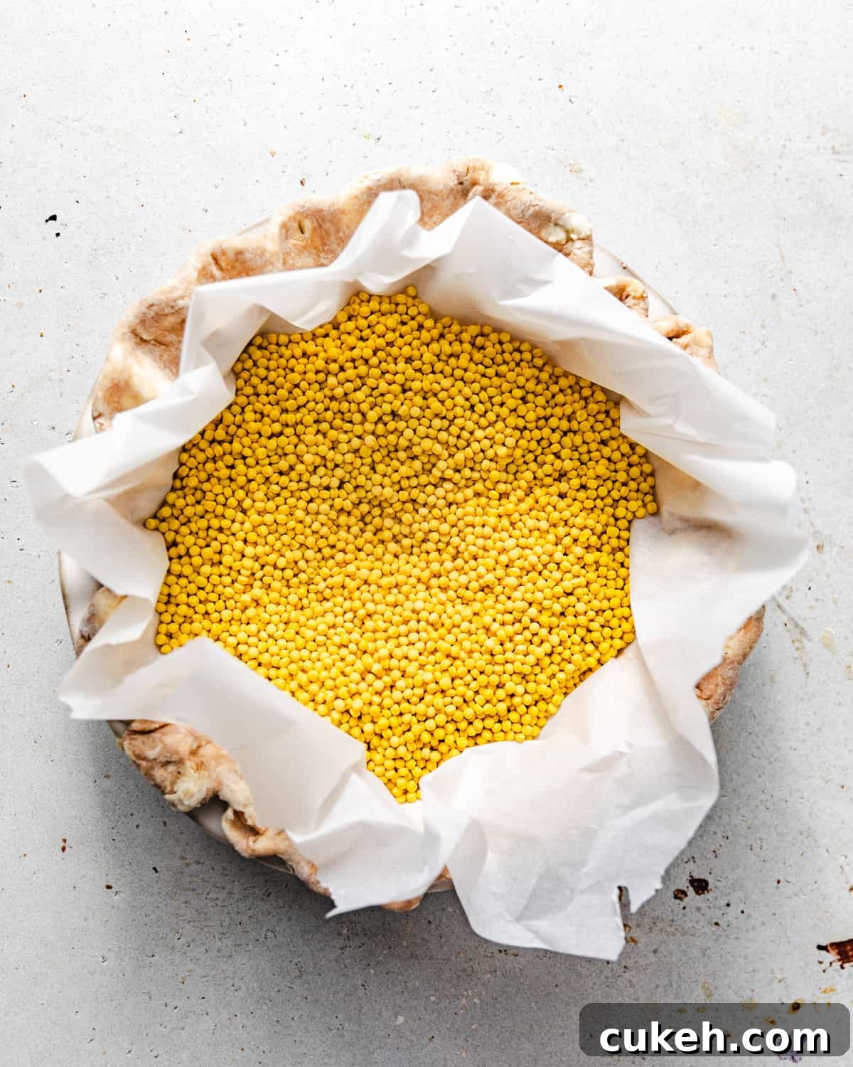 pie crust in a pie dish with pie weights filling the center in parchment paper.