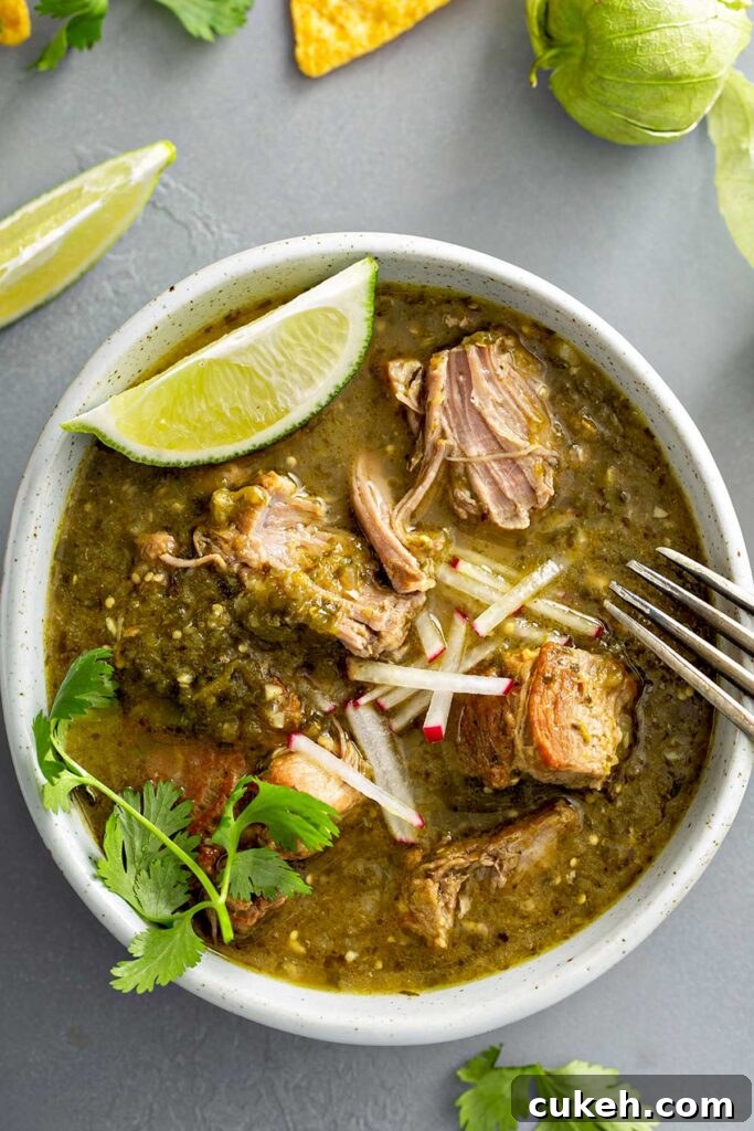 A bowl of pork chile verde stew with pieces of pork so tender that are getting shred by a fork 