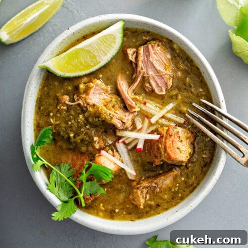 tender pieces of stewed pork in chile verde sauce getting shred with a fork