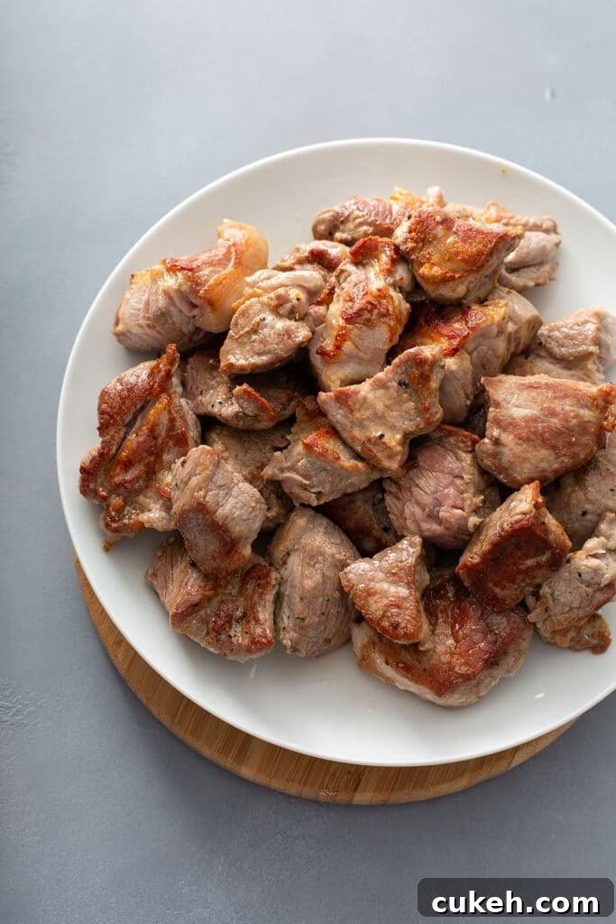 Perfectly seared pork pieces transferred onto white plate.