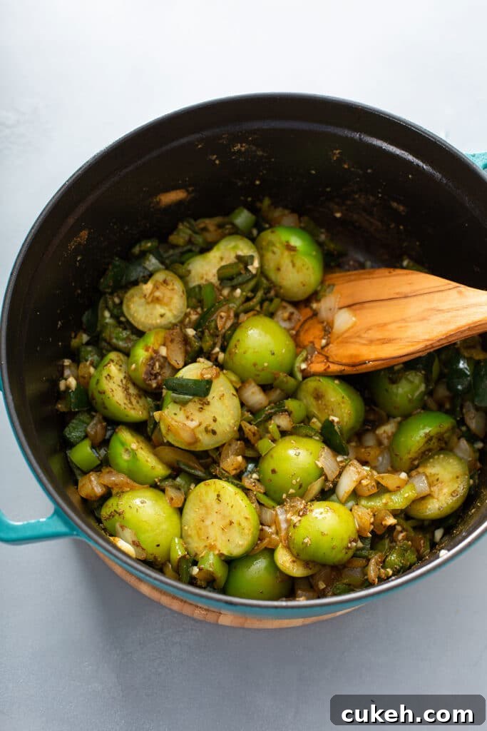 Beautifully seasoned peppers and tomatillos being stirred in dutch oven pot with a wooden spatula 