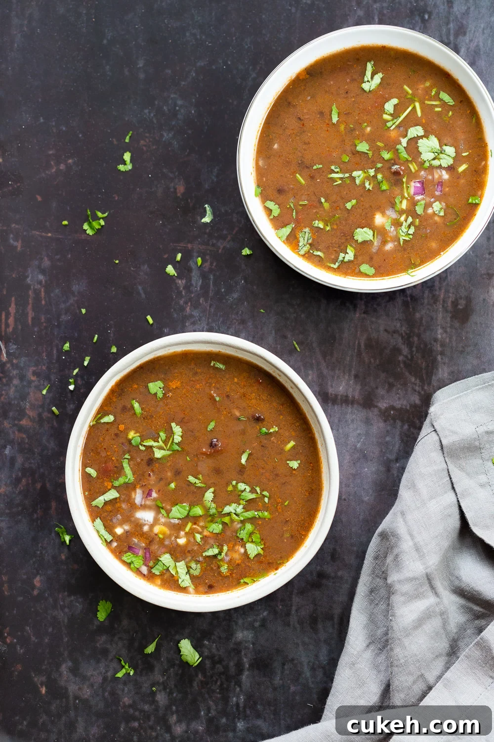 overhead shot of two bowls of vegan black beans soup sprinkled with chopped herbs 