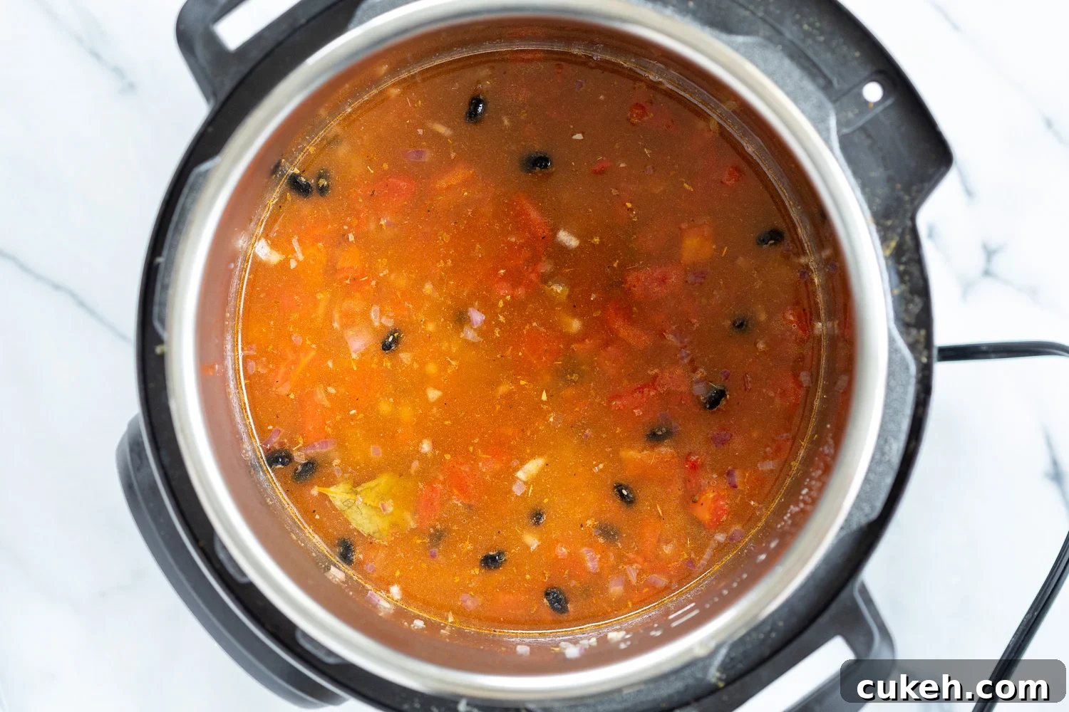 dried soaked beans being added to an Instant Pot filled with seasoned tomato broth